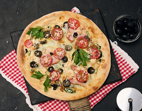 Baked pizza with chicken, tomatoes and olives on a black table