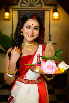 Portrait of beautiful Indian woman wearing traditional red and white saree and jewellery, holding a plate of religious offerings