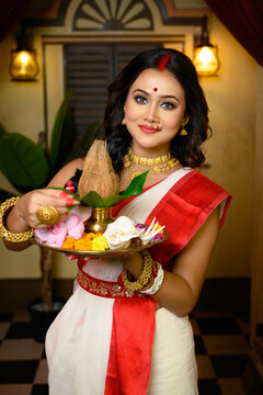 Portrait of beautiful Indian woman wearing traditional red and white saree and jewellery, holding a plate of religious offerings