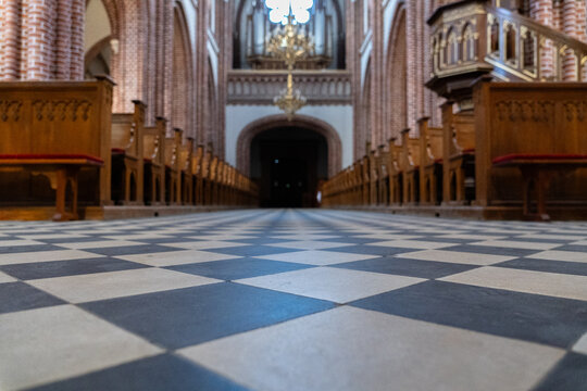 Gothic brick church interior with ornate chandeliers, pipe organ and checkerboard floor, historic European religious architecture	
