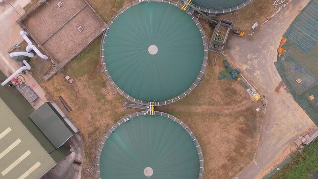 Aerial drone view straight down and rising at a waste water treatment plant with green anaerobic digester tanks providing power for the facility