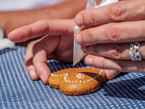 Hands Decorating Heart-Shaped Gingerbread Cookie With White Icing Bag During Holiday Baking