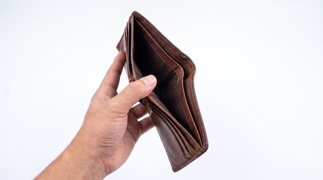 A person's hand holds an open, empty brown leather wallet, symbolizing financial emptiness, poverty, or being broke against a plain white background.