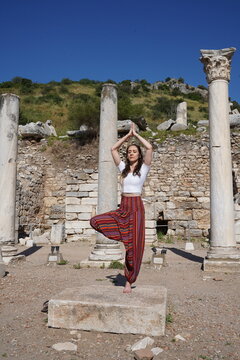 Woman practicing yoga tree pose among ancient columns in Ephesus