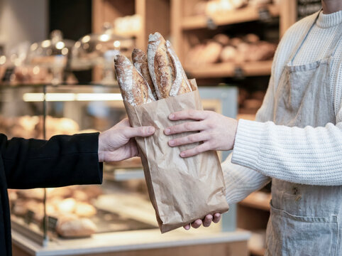 Baker handing fresh baguettes to customer in bakery