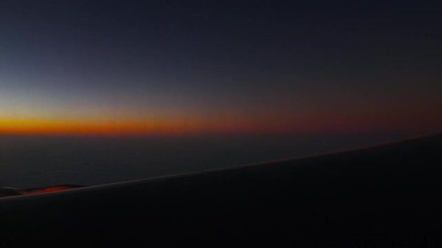 Airplane wing flying above cloud layer during colorful sunset at high altitude, scenic view from passenger window at dusk with orange sky gradient