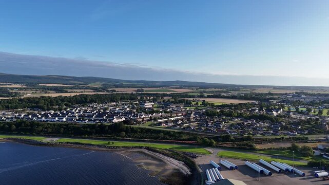 High wide aerial drone shot panning over Invergordon town toward offshore jack-up oil rig legs in Cromarty Firth Scotland