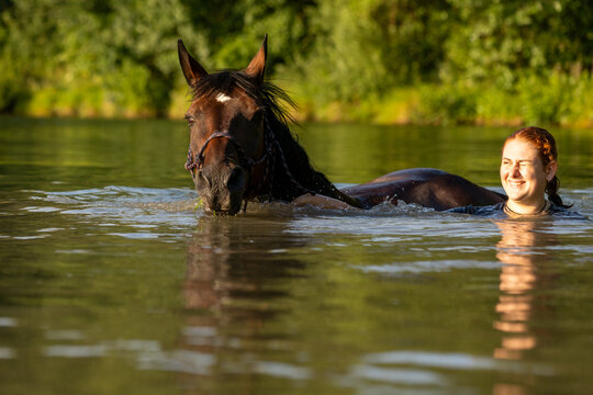 Reiterin badet mit Pferd im See