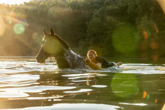 Reiterin badet mit Pferd im Gegenlicht