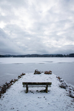 Snow-covered wooden bench overlooking frozen Settons lake in winter, Morvan regional park, Burgundy, France