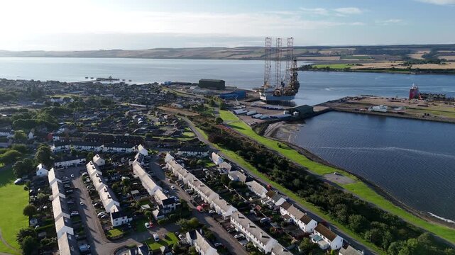 High wide aerial drone video tracking over Invergordon residential neighborhood towards port and Cromarty Firth