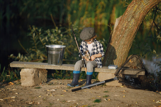 Blonde curly boy sitting on a bench and holding a fishing rod