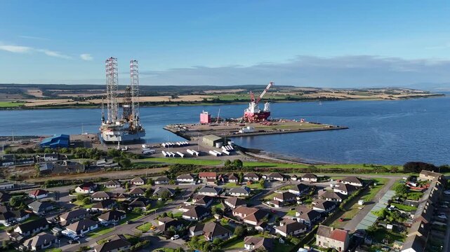Wide angle aerial drone view of Invergordon residential neighborhood, oil rig, and industrial port at Cromarty Firth, Scottish Highlands, Scotland, UK