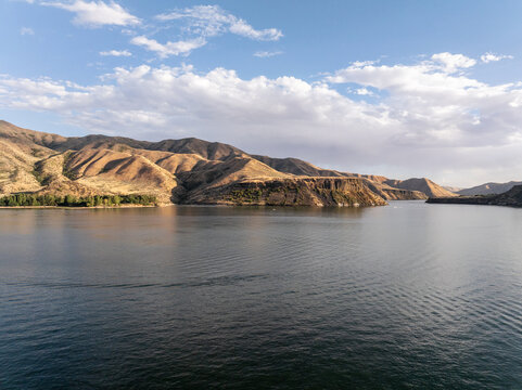 Aerial view of tranquil lake surrounded by undulating hills under partly cloudy