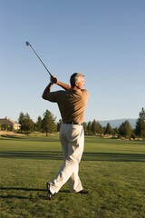 Obraz premium Mature man finishing golf swing on a manicured course with long shadow for banner and background design