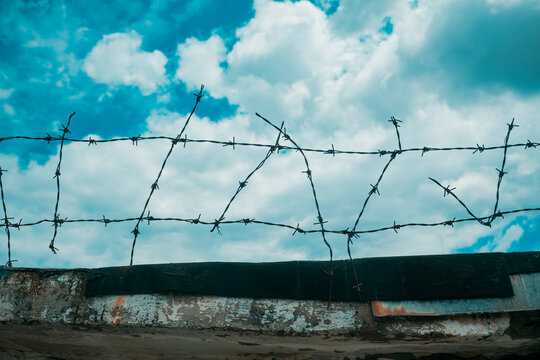 Rusty barbed wire fence stretches across a dramatic cloudy sky, evoking themes of security, confinement, isolation, danger and boundary in a stark outdoor landscape.