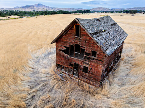 Deserted barn-like building in golden grassland with hills behind