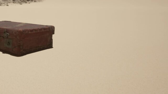 A vintage suitcase is resting on soft sand with no other objects around. The scene is illuminated by bright sunlight, and the background is empty, creating an isolated feeling.