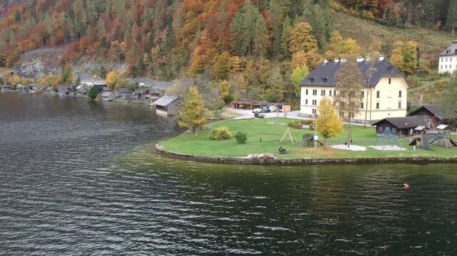 Hallstatt Austria seen by drone with an elegant lakeside building, calm Alpine water and vivid autumn trees creating a picturesque Salzkammergut landscape.