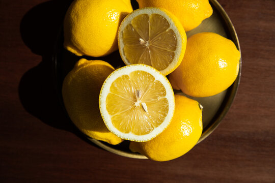 Plateau de citrons jaunes empil&eacute;s en gros plan, cinq citrons entiers et un coup&eacute; en deux, plateau couleur bronze pos&eacute; sur une table brun fonc&eacute;, image contrast&eacute;e et lumineuse, vue du dessus
