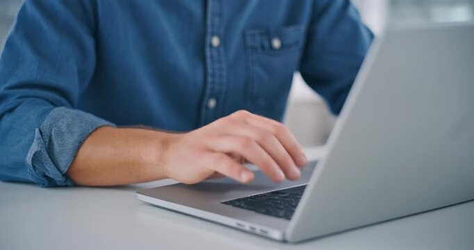Close up of male hands typing on laptop in denim shirt at work desk.