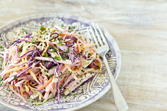 Cabbage and carrot salad, or coleslaw, on a pretty lavender plate with a fork and soft pastel background