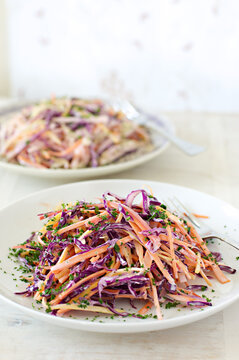 Plate of purple cabbage and carrot salad, or coleslaw, in the foreground, with another blurred in the background 