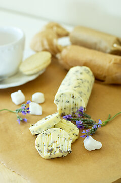 Slices of fresh, homemade herbed butter with lavender, sugar cubes and a cup in the blurred background