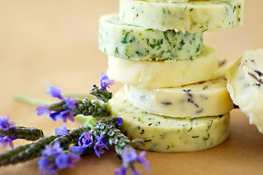 Slices of home-made assorted herbed butter, styled with a sprig of lavender, selective focus, blurred background 