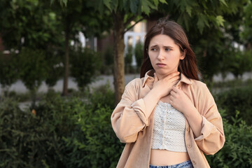 Naklejka premium Sore throat and health issues, young woman touching her neck with discomfort outdoors, medical symptoms and illness