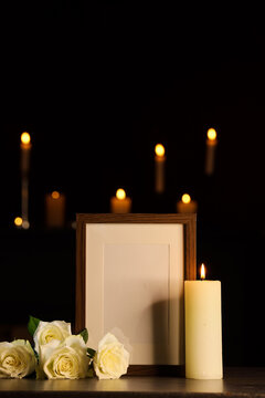 Grief and remembrance, blank photo frame with white roses and a burning candle in a dark setting