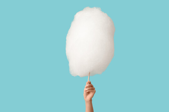 Female hand with stick of tasty cotton candy on color background
