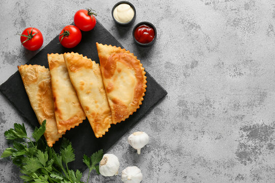 Board with tasty chebureks, fresh vegetables and sauces on grey grunge table