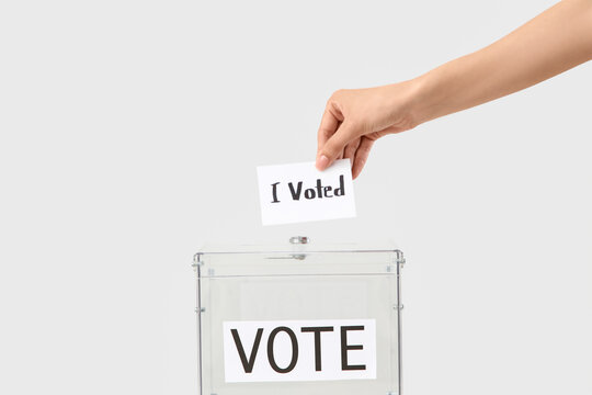 Female hand holding paper with text I VOTED near ballot box on light background
