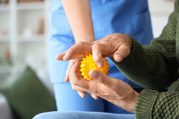 Obraz premium Senior man suffering from Parkinson syndrome with massage ball and nurse at home, closeup