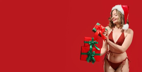 Naklejka premium Smiling woman in Santa hat holding Christmas gifts in bikini