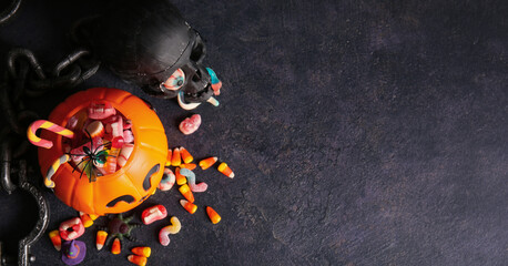 Halloween celebration and trick or treat concept, pumpkin bucket filled with candy, skull and chains on dark background © Pixel-Shot