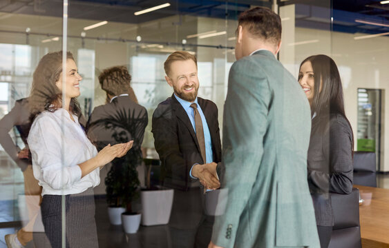Business colleagues handshake during team meeting agreement. In a modern office, partnership leads to a contract as coworkers applaud showing success and teamwork. Clear concept of deal success.