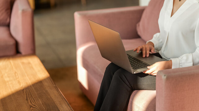 Woman working on laptop while sitting on a comfortable pink sofa in a bright room
