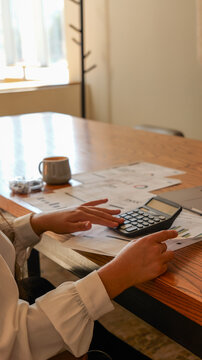 Woman's hands using a calculator on a wooden desk with papers and coffee