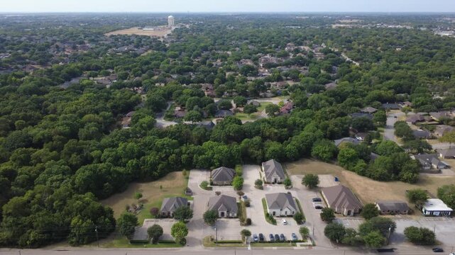 Commercial building clusters border hardwood woodland corridors off E Pleasant Run Road. Distinct hip rooflines overlook manicured parking lots, distant civic water towers, DeSoto, TX