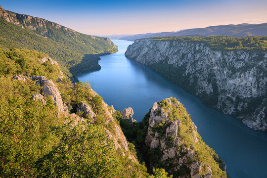 Sweeping high-angle view down jagged rocky spires into the deep Danube River canyon at Iron Gates, Serbia and Romania border, flanked by lush summer cliffs. Destination concept
