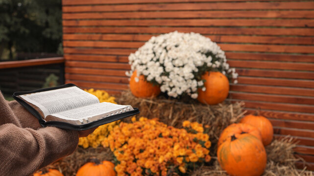 Person holding an open bible amidst autumn decorations with pumpkins and mums