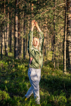 Woman walking through autumn pine forest, breathes in the forest air and raising both hands together while enjoying pleasant weather, peaceful outdoor recreation, relaxation and connection with nature