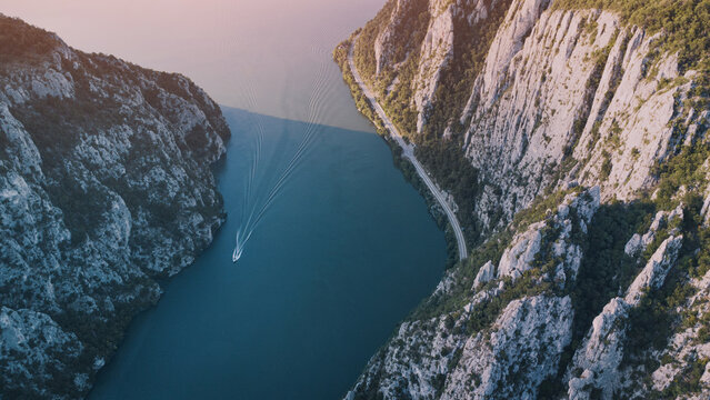 Boat navigating the Danube River through the Iron Gates gorge, surrounded by towering cliffs and a scenic road