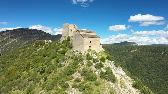 Drone footage of the historic Samitier Castle perched on a rocky ridge surrounded by lush green hills and mountains in the Aragon region of Spain. No people are visible in the scene.