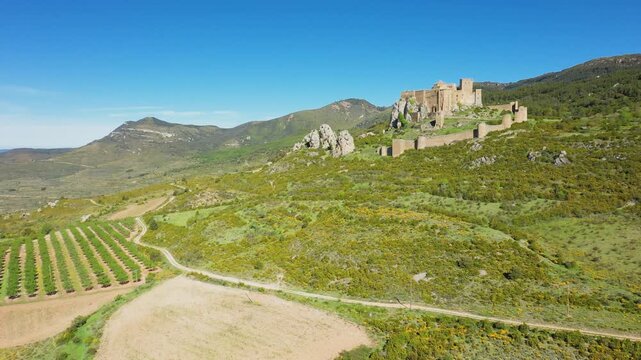 Aerial footage showcasing the medieval Loarre Castle perched on a hilltop, surrounded by green fields, farmland, and rolling hills in the Huesca province of Aragon, Spain.