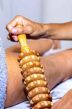 Professional therapist performing maderotherapy massage on leg using wooden roller