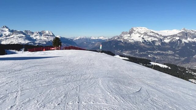 Wide panoramic view of a snow-covered ski slope at Megeve in the French Alps, Haute-Savoie, France. The video shows a clear blue sky, distant snow-capped mountains, and ski tracks on the slope.