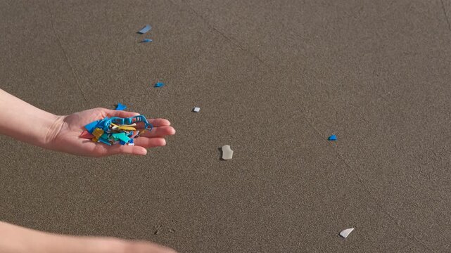 Volunteer collecting microplastic waste on sandy beach. Young environmental activist picking up colorful microplastic and nurdles from the sand, demonstrating the serious problem of water pollution